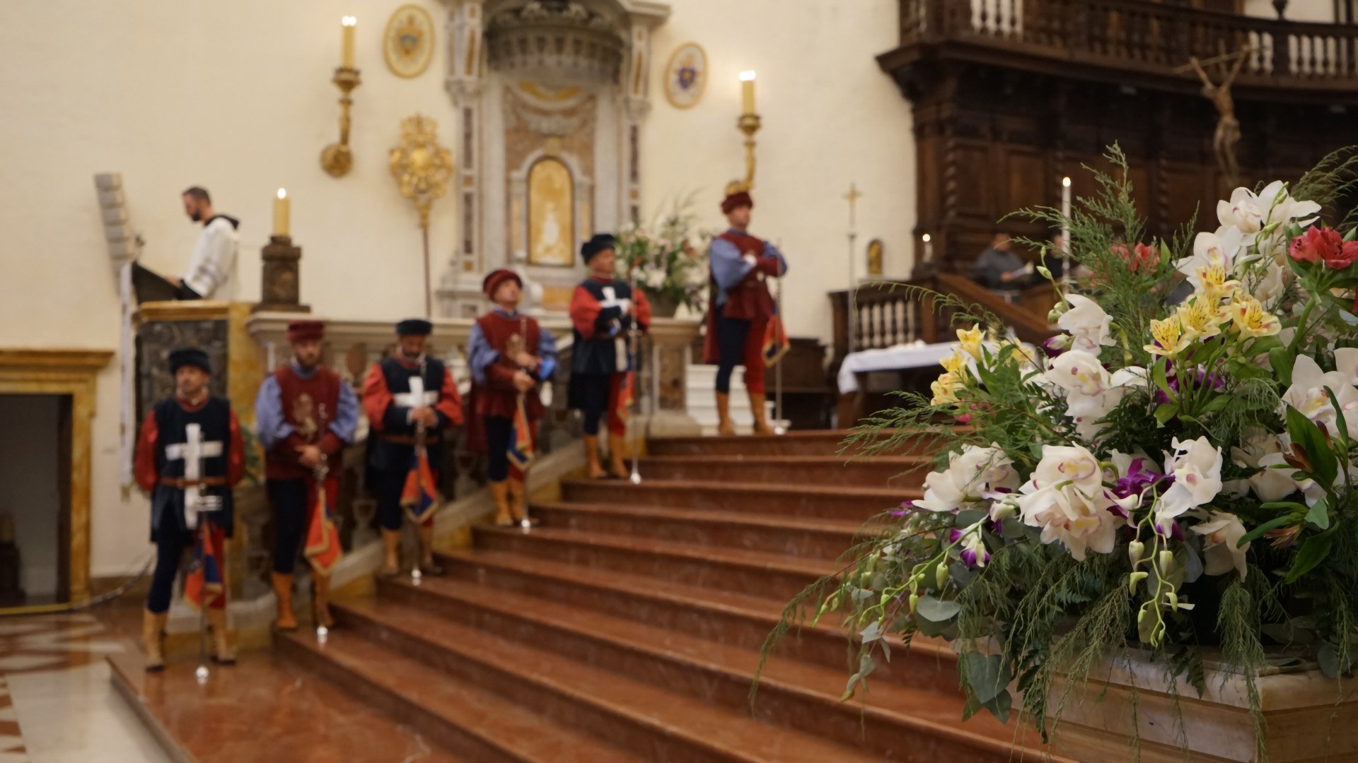 La foto rappresenta l'interno di una basilica con dei trombettieri vestiti in maniera medievale che assistono alla festa del perdono di Assisi.