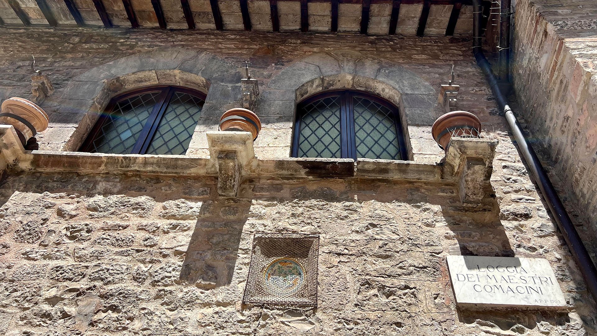 Dettaglio della Loggia dei Maestri Comacini. Nello specifico il dettaglio del cartello in marmo con inciso il nome della Loggia e le finestre della stessa con una texture a rombo nella parte esterna dei vetri fatta in ferro.