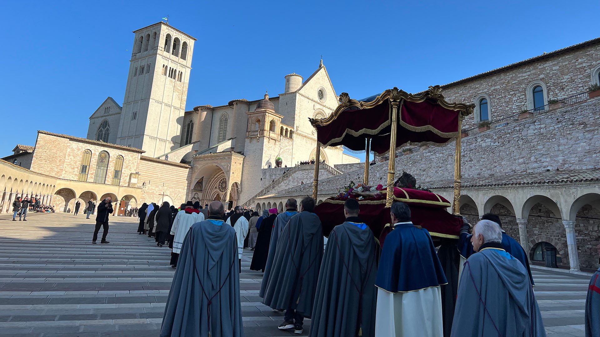 La foto rappresenta la parte inferiore della Basilica Papale di San Francesco dove si sta svolgendo la celebrazione della settimana santa. Nel corteo possiamo vedere un altarino coperto da un tessuto rosso orlato d'oro.